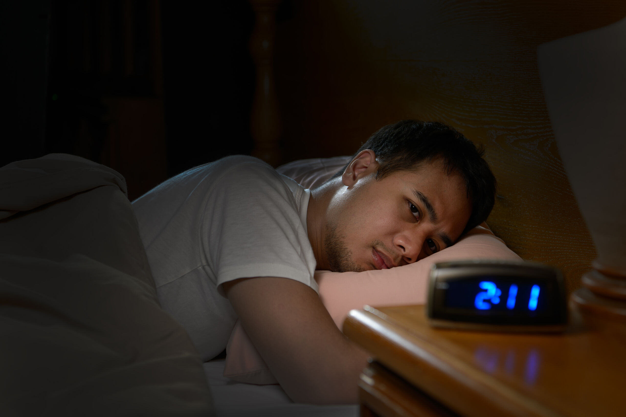 Mensch liegt schlaflos im Bett und schaut den Wecker an, der 2:11 in der Früh zeigt.